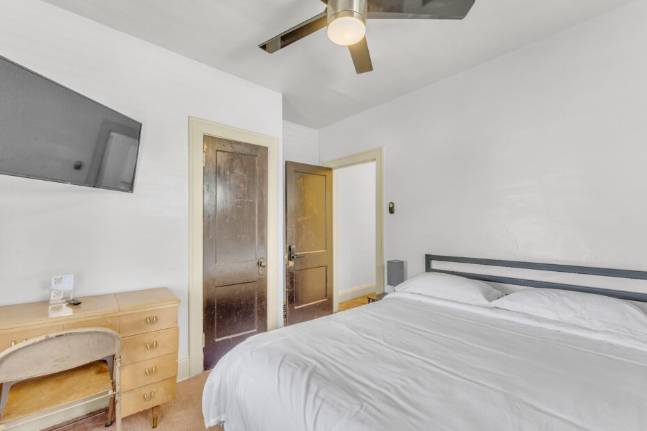 P3769 R4 bedroom with white bedding, desk, television and wooden entrance door.