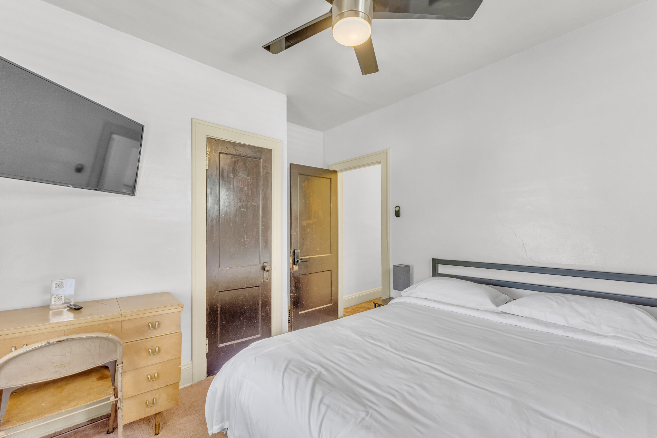 P3769 R4 bedroom with white bedding, desk, television and wooden entrance door.